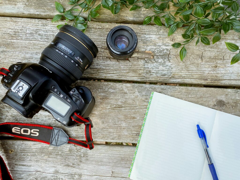 Camera, lens and open notebook on a wooden table.
